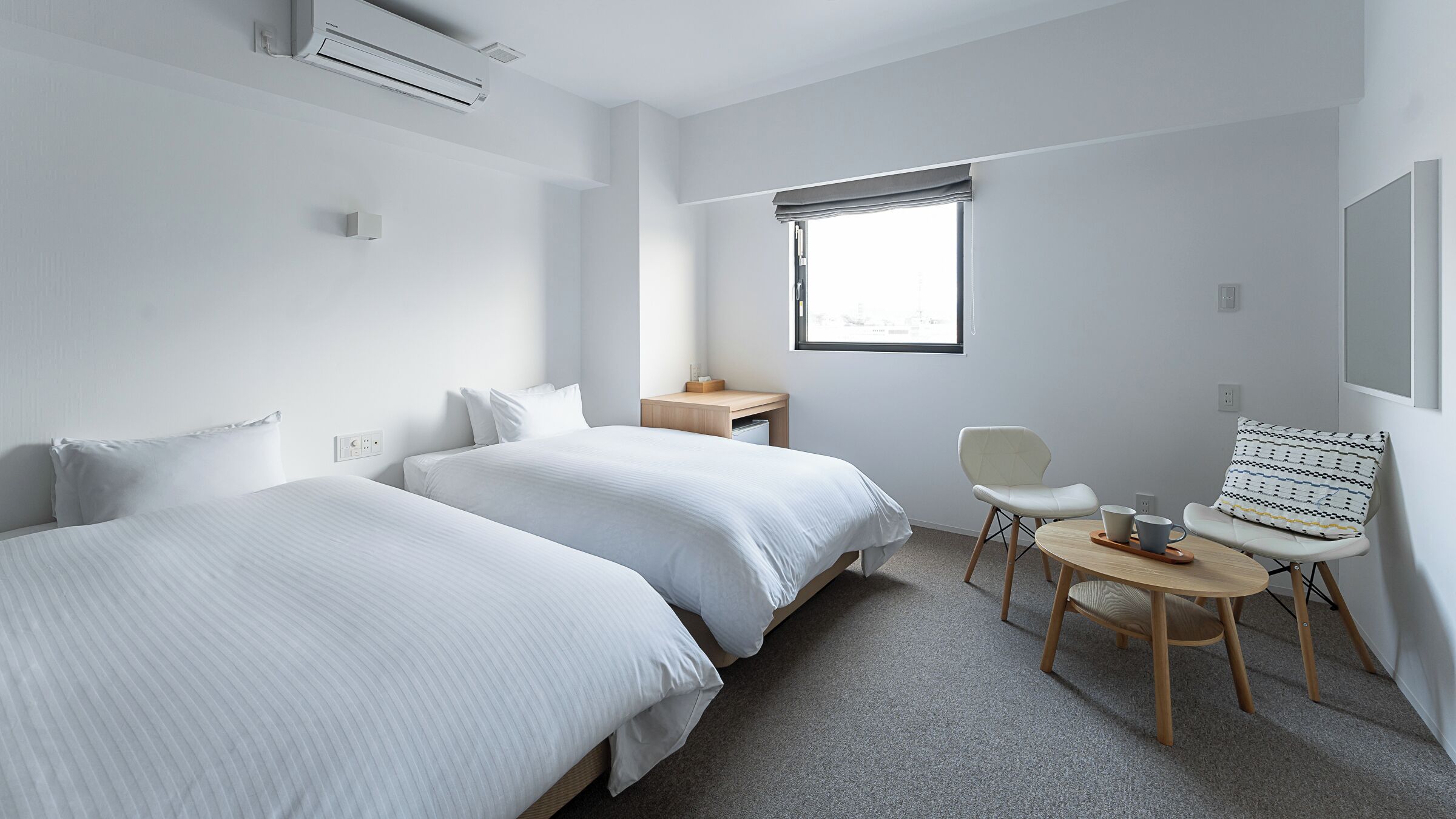 Hotelkamer met twee bedden, een kleine tafel, een stoel, een raam met uitzicht en een airconditioning.