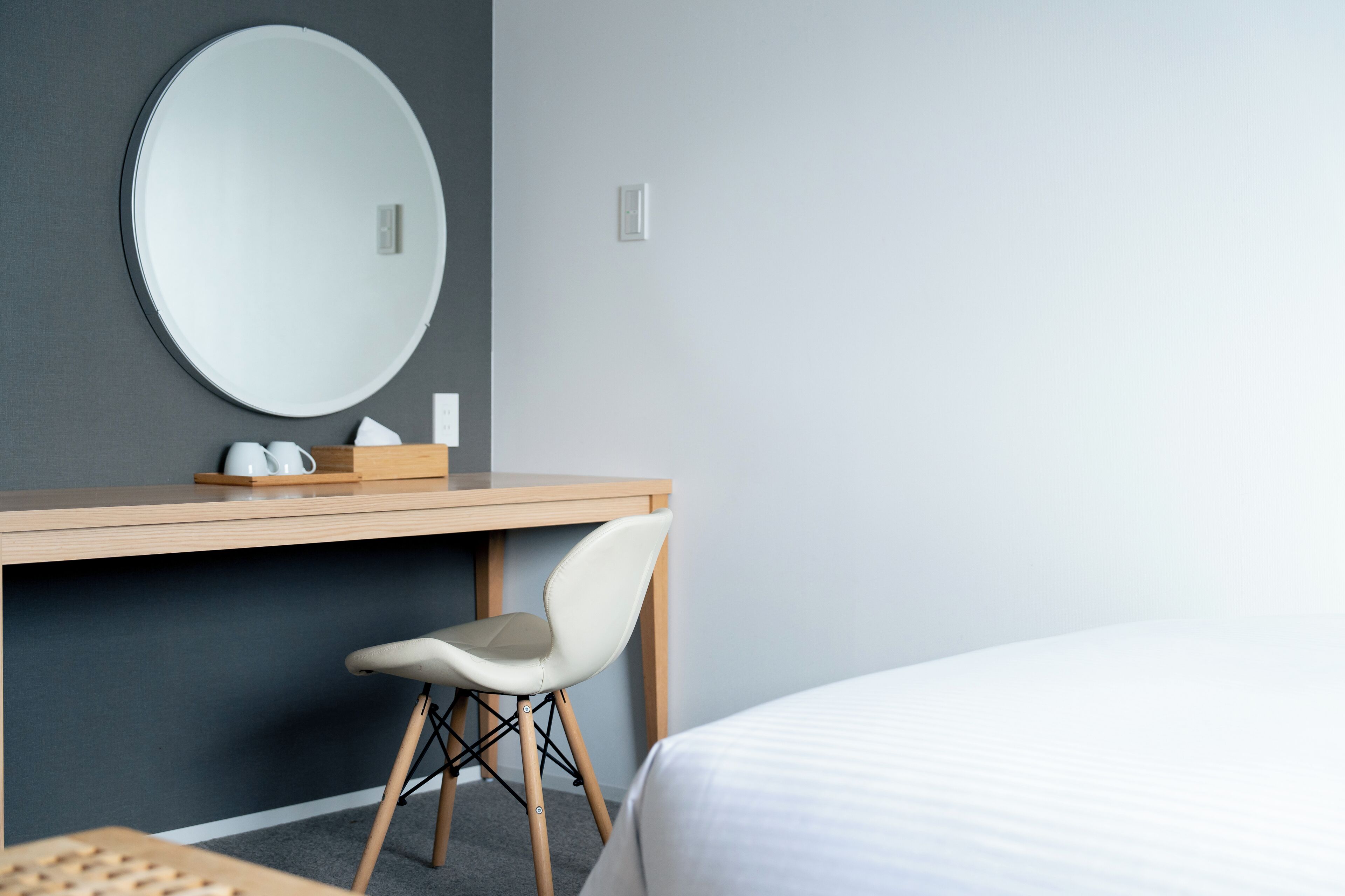 Ein Hotelzimmer mit einem Bett, einem Schreibtisch mit Stuhl, einem runden Spiegel und einem kleinen Tisch mit Krug und Tassen.