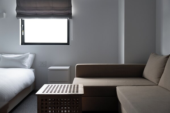 A modern hotel room with a bed, a sofa, a small table, and a window with a view.