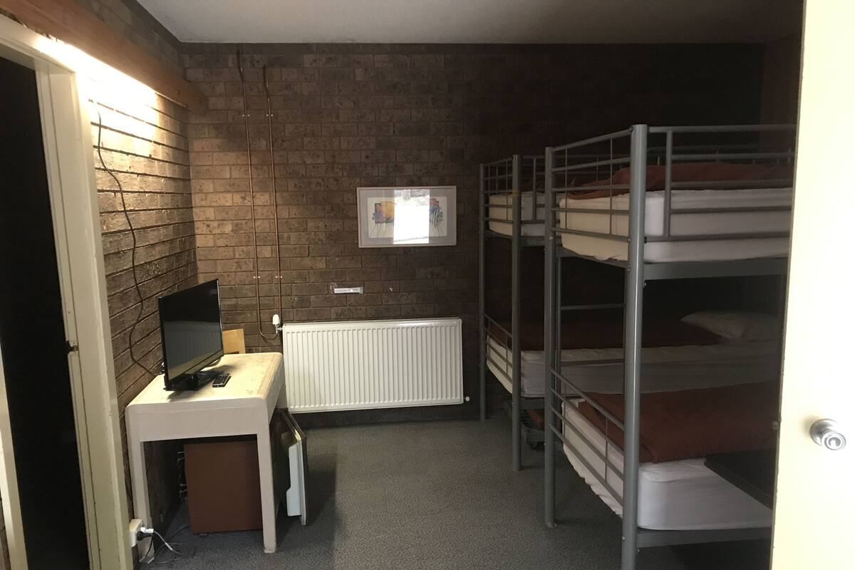 Een studentenkamer met stapelbedden, een bureau met computer, een radiator en een lijst met een foto.