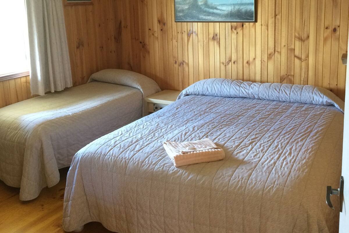 Een kamer met houten paneelwanden, twee eenpersoonsbedden, een groot bed, een schilderij en een raam met gordijnen.