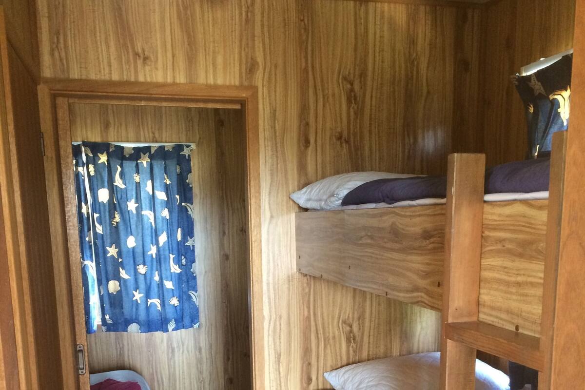 Een slaapkamer met stapelbedden, een houten inrichting, een deur naar een andere kamer en een gordijn met een stermotief.