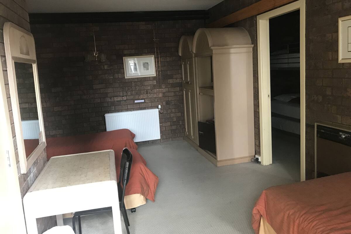 Een kleine kamer met twee bedden, een radiator, een tafeltje en een kledingkast.