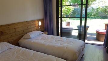 A room with two beds, a wooden headboard, a large sliding glass door leading to an outdoor area with wicker furniture.