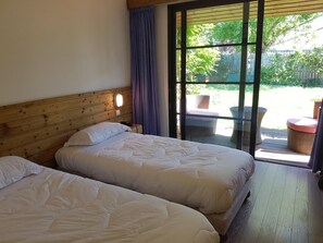 A room with two beds, a wooden headboard, a large sliding glass door leading to an outdoor area with wicker furniture.