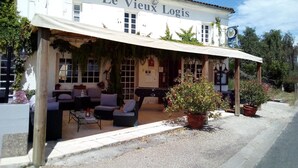 Un edificio llamado "Le Vieux Logis" con mesas al aire libre y plantas en macetas.