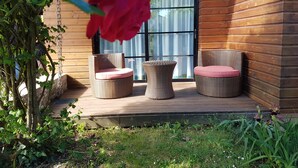Una terraza de madera con sillas de mimbre y un ventanal de vidrio.