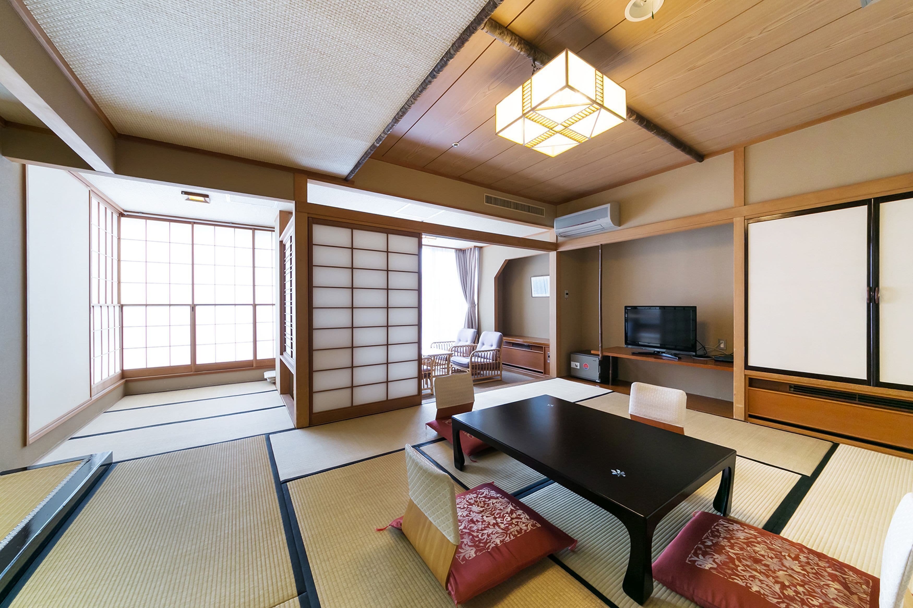 Ein traditioneller japanischer Raum mit Tatami-Boden, einem niedrigen Tisch, Kissen, einem Fernseher und Schiebetüren.
