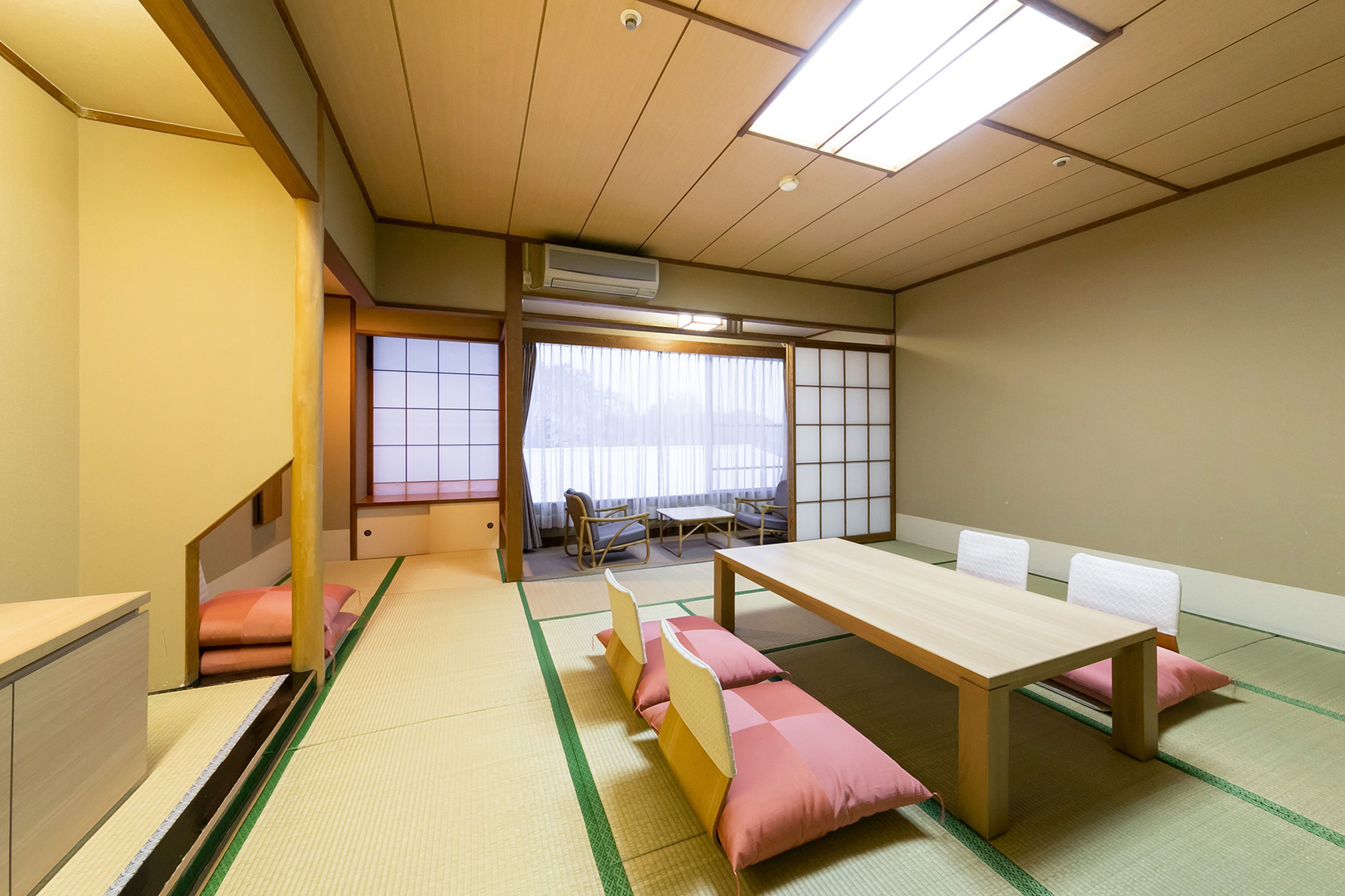 A tatami mat room with a low table and cushions, a sliding door, and a view through a window.