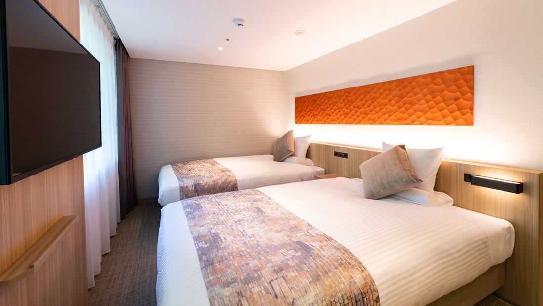 A hotel room with two beds, a flat-screen TV, a large orange wall art piece, and a wooden headboard.