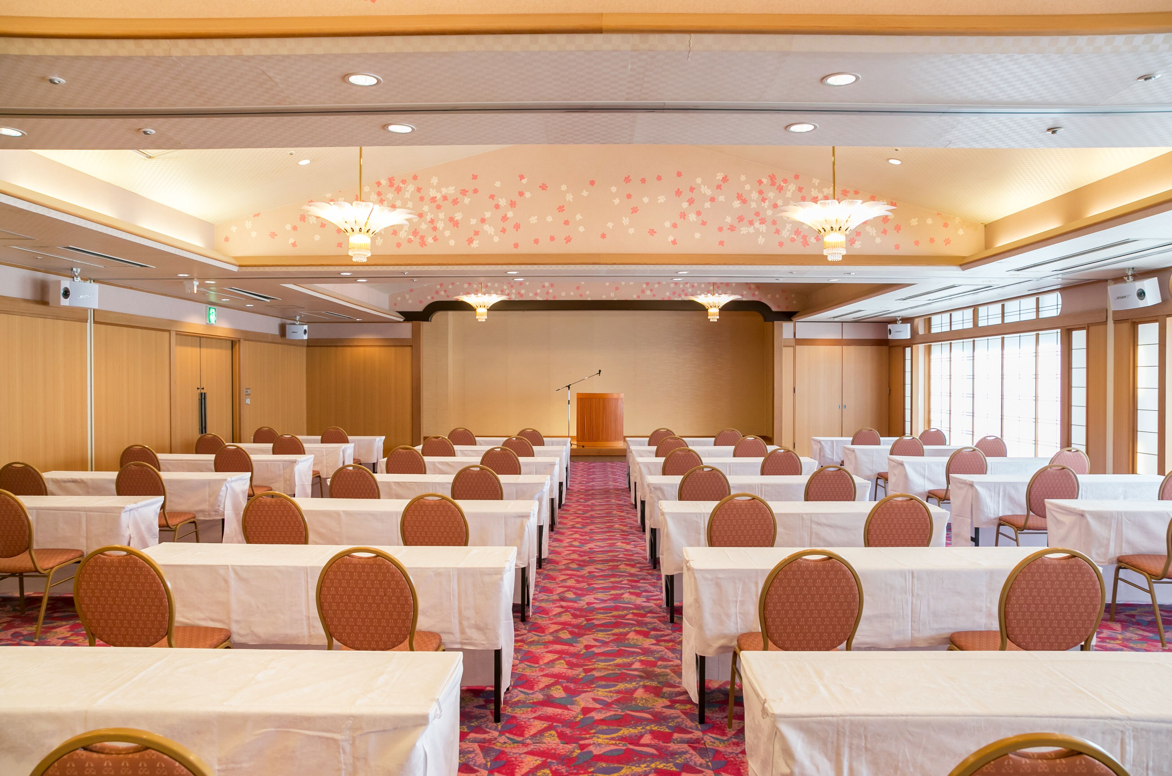 A conference room with rows of tables and chairs, a podium, and large windows.