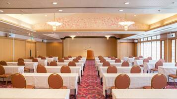 A conference room with rows of tables and chairs, a podium, and large windows.