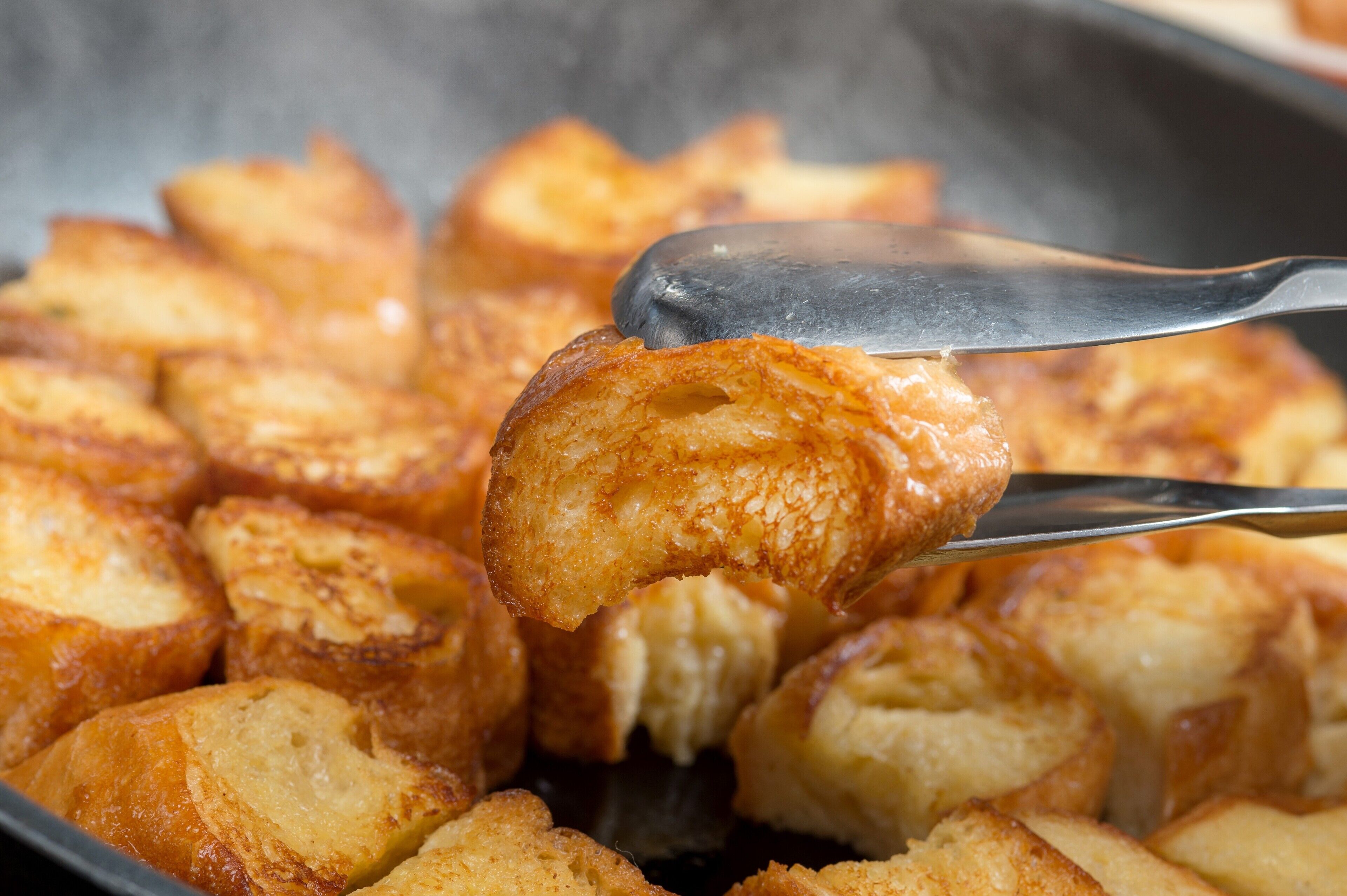 A close-up of golden-brown toast being lifted with tongs.