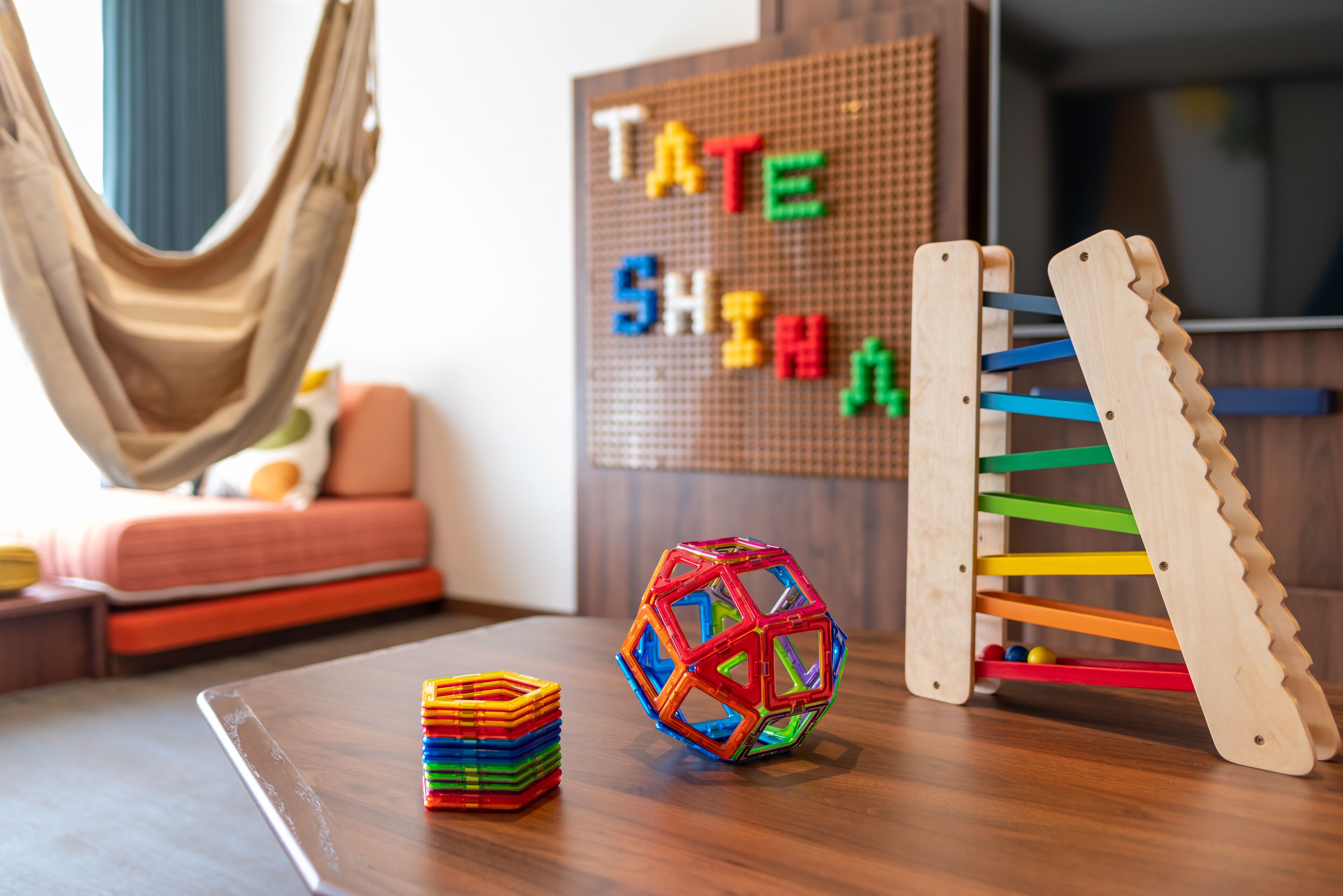 A room with a hammock, a colorful ball, a wooden rack, and a pegboard with letters.