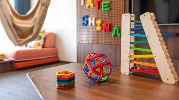 Una habitación con una hamaca, una pelota de colores, un estante de madera y un tablero de anuncios con letras.