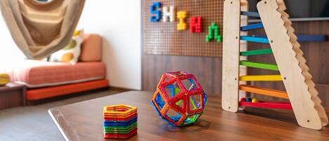 A room with a hammock, a colorful ball, a wooden rack, and a pegboard with letters.