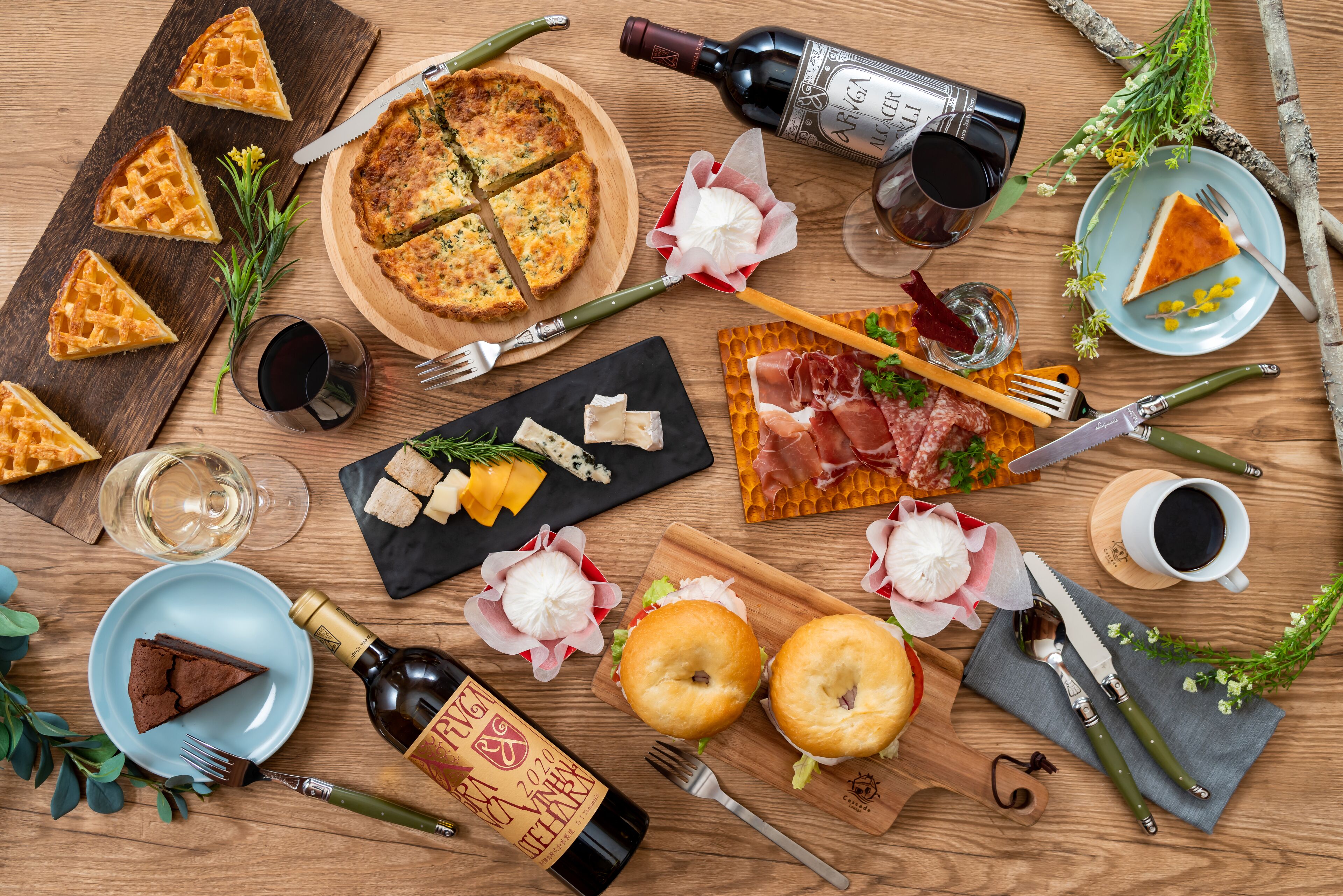 Une table en bois sur laquelle sont disposés divers aliments, notamment des gaufres, une quiche, du fromage et de la viande, ainsi que des bouteilles de vin et une bouteille de champagne.