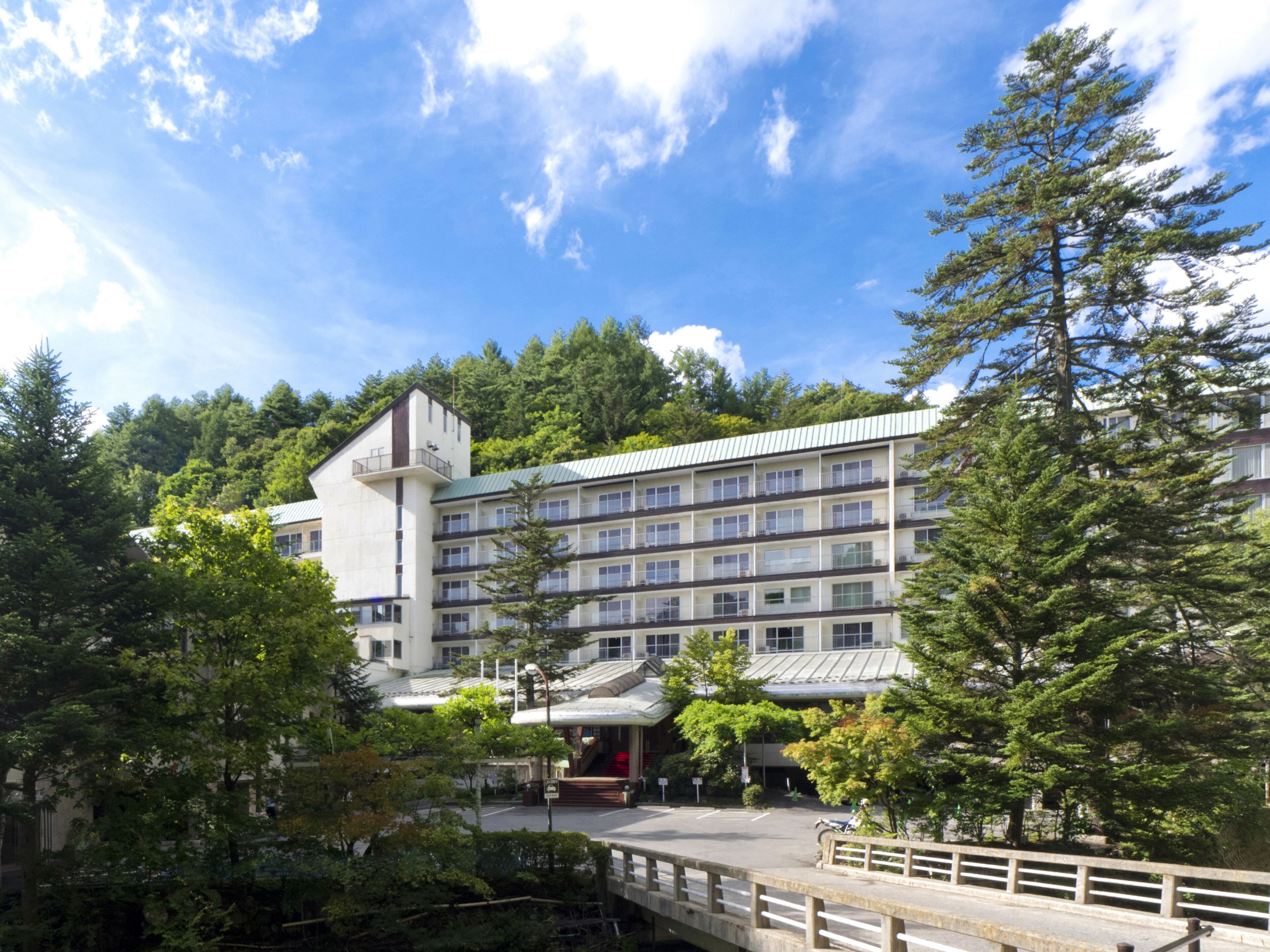 Um hotel de vários andares com um pátio central, rodeado por árvores e uma ponte.