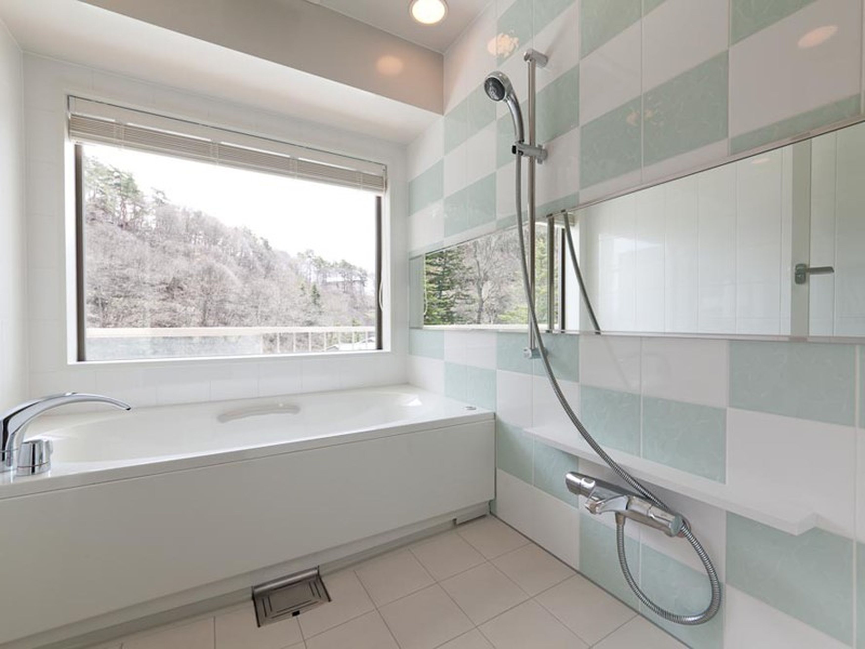 A modern bathroom with a large bathtub, a shower, and a window providing a view of trees.