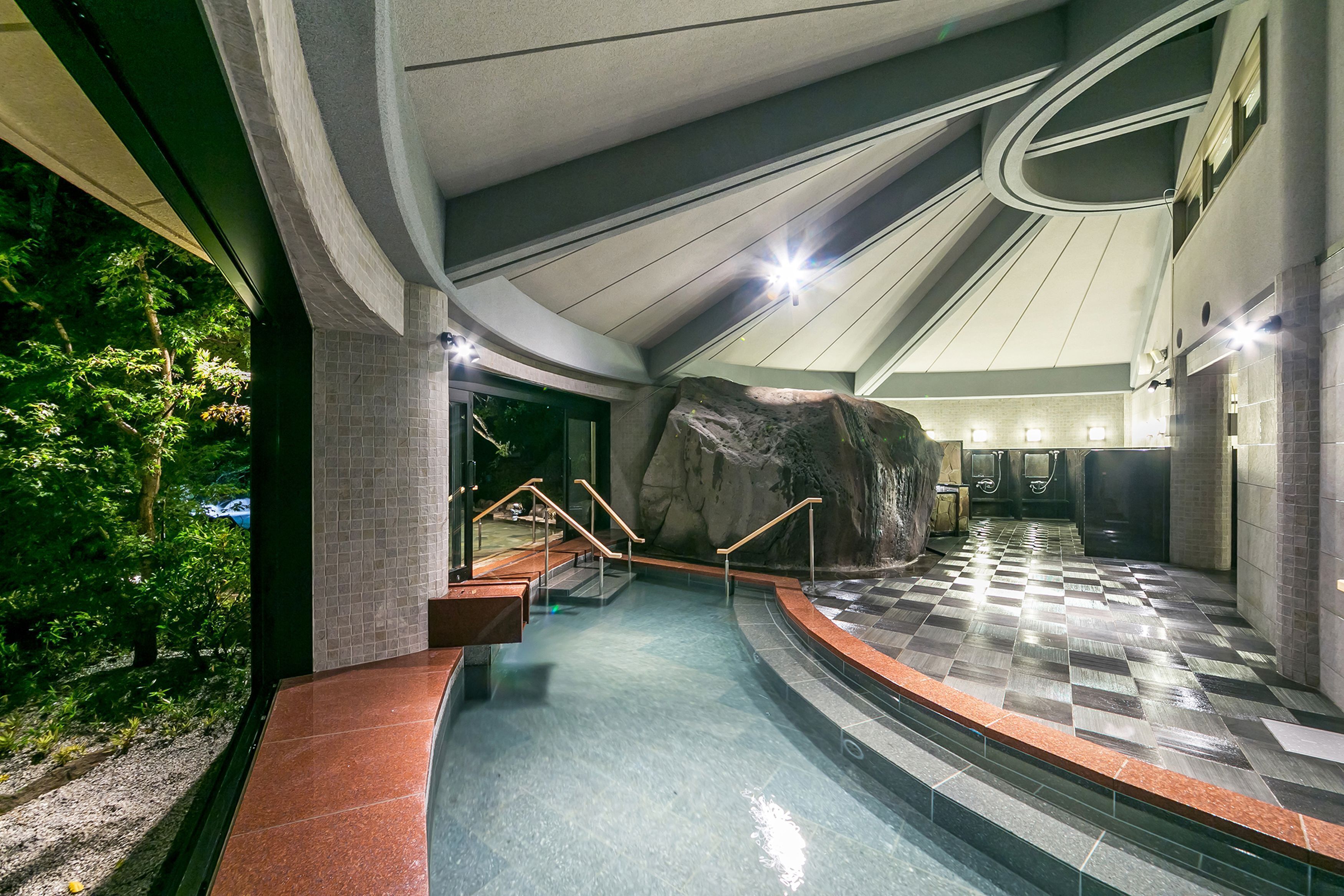 A modern indoor pool area with a large rock feature, tiled flooring, and a curved ceiling design.