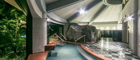A modern indoor pool area with a large rock feature, tiled flooring, and a curved ceiling design.