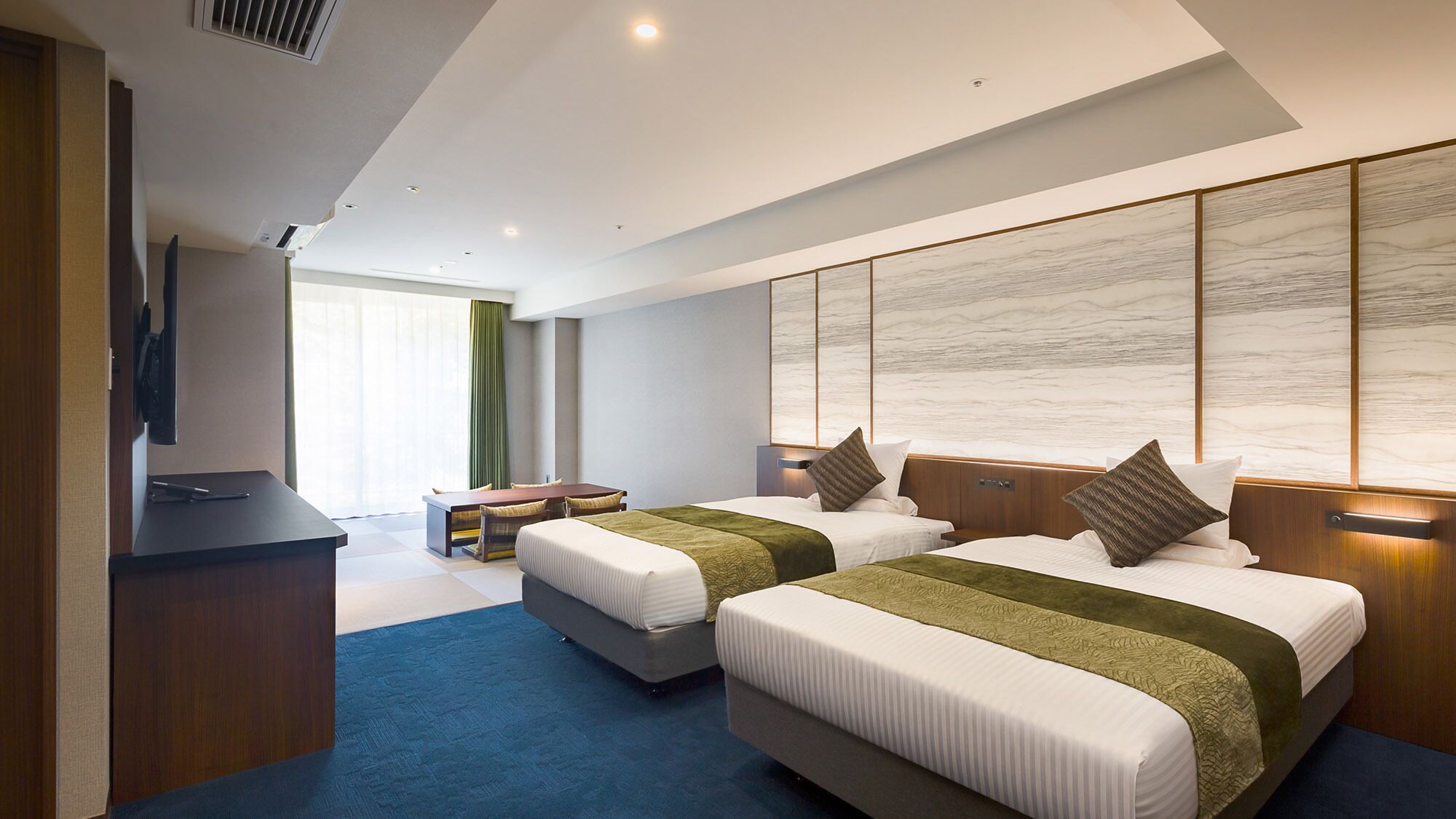 Quarto de hotel moderno com duas camas, uma escrivaninha e uma janela grande.