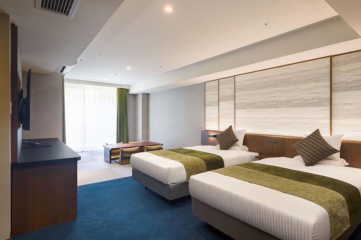 Quarto de hotel moderno com duas camas, uma escrivaninha e uma janela grande.