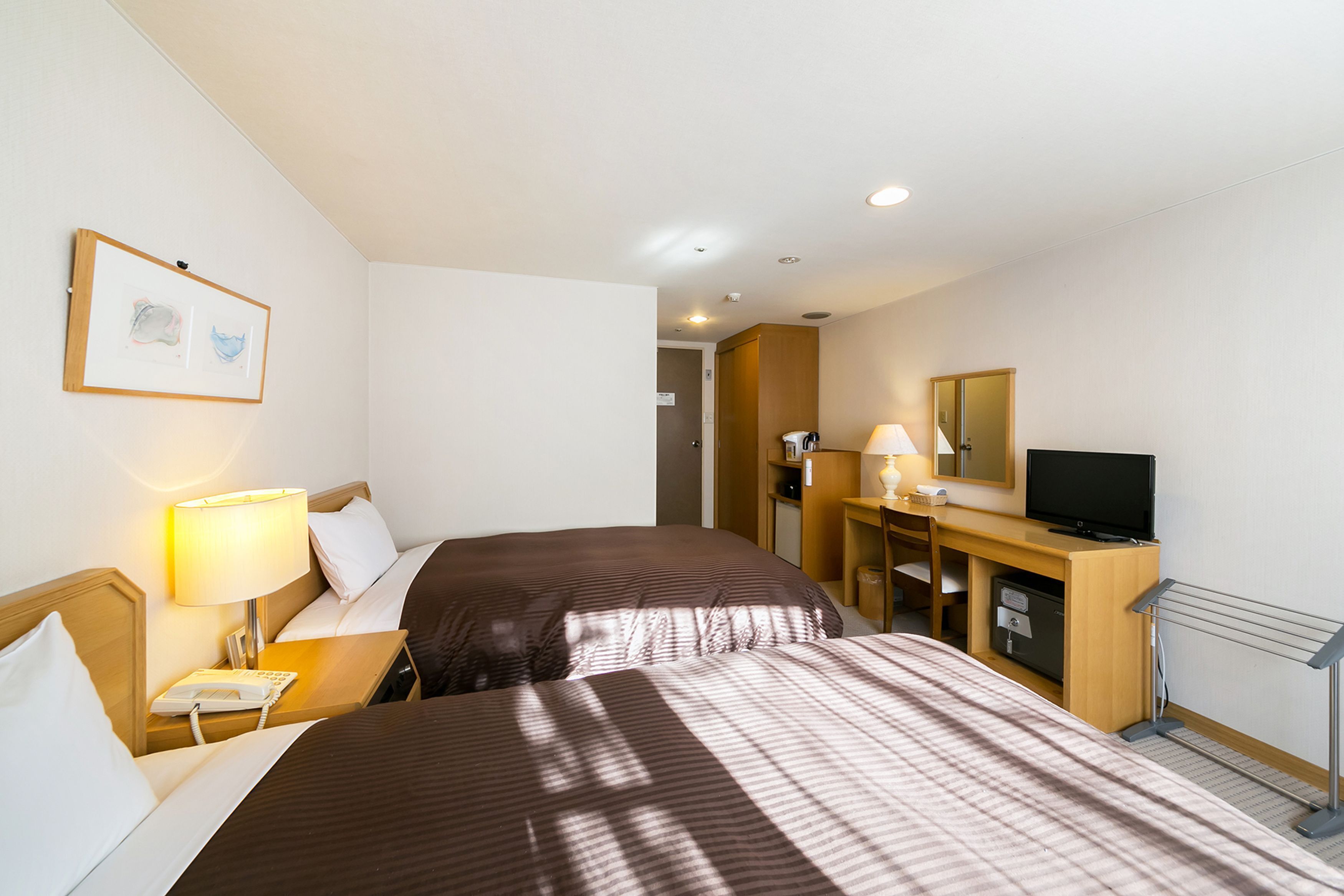 A hotel room with two beds, a desk with a lamp, a television, and a mirror.
