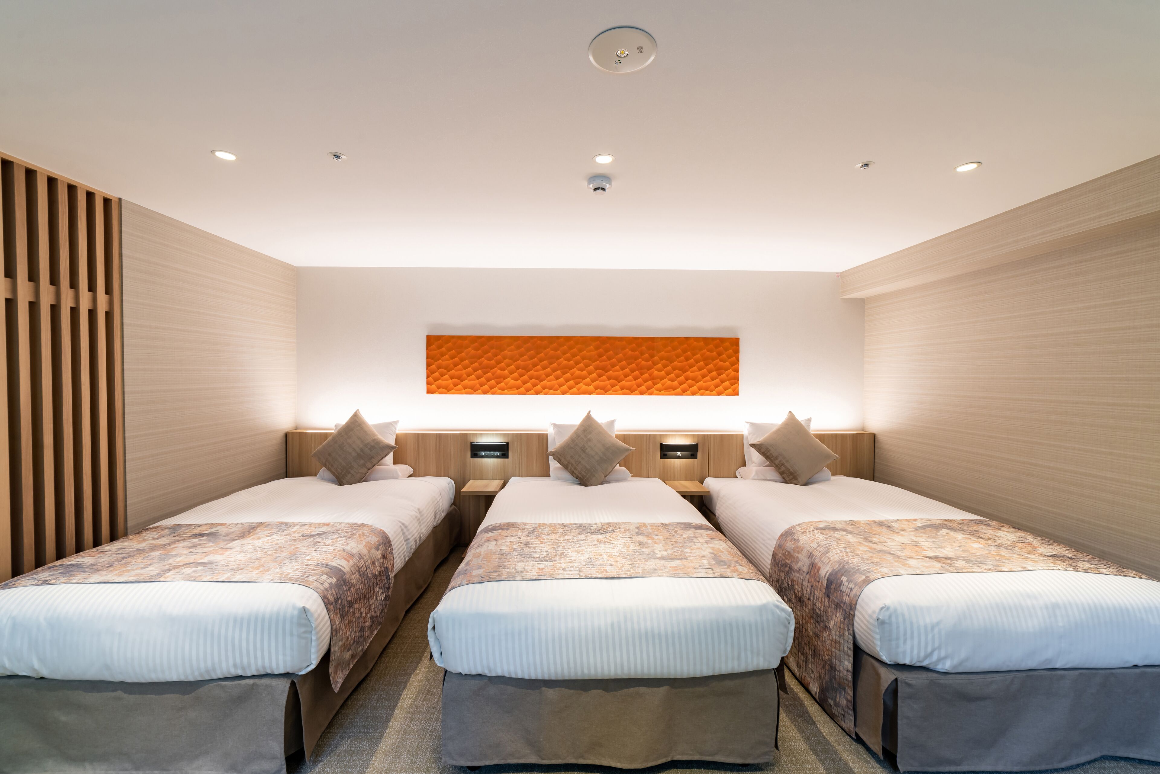 A hotel room with two beds, a large orange wall panel, and recessed ceiling lights.