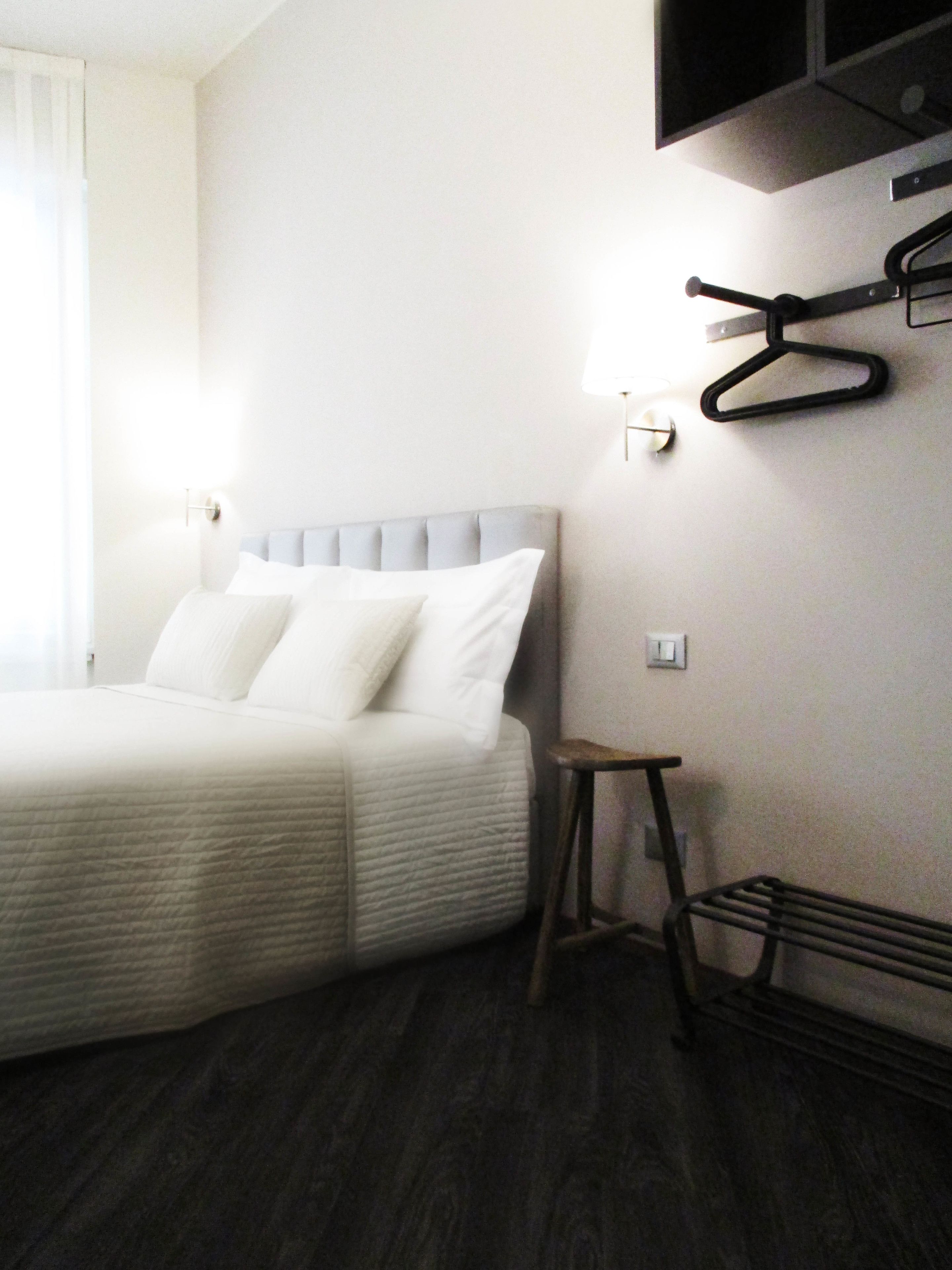 Une chambre d’hôtel avec un lit, un petit tabouret et un téléviseur fixé au mur.