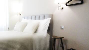 Une chambre d’hôtel avec un lit, un petit tabouret et un téléviseur fixé au mur.