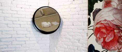 Un baño con pared de ladrillo blanco, un espejo redondo, un lavamanos blanco y una lámpara colgante.