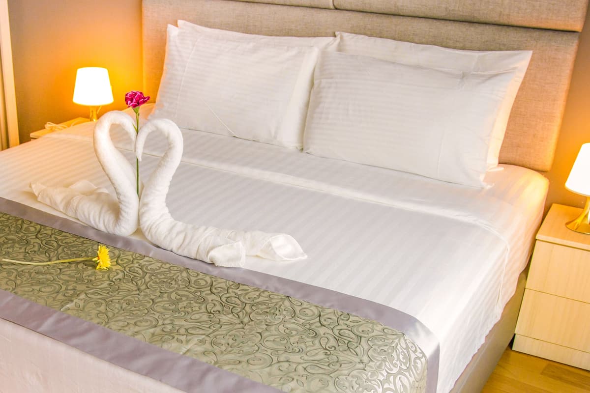 A neatly made bed with a decorative towel arrangement, a bedside lamp, and a floral decoration.