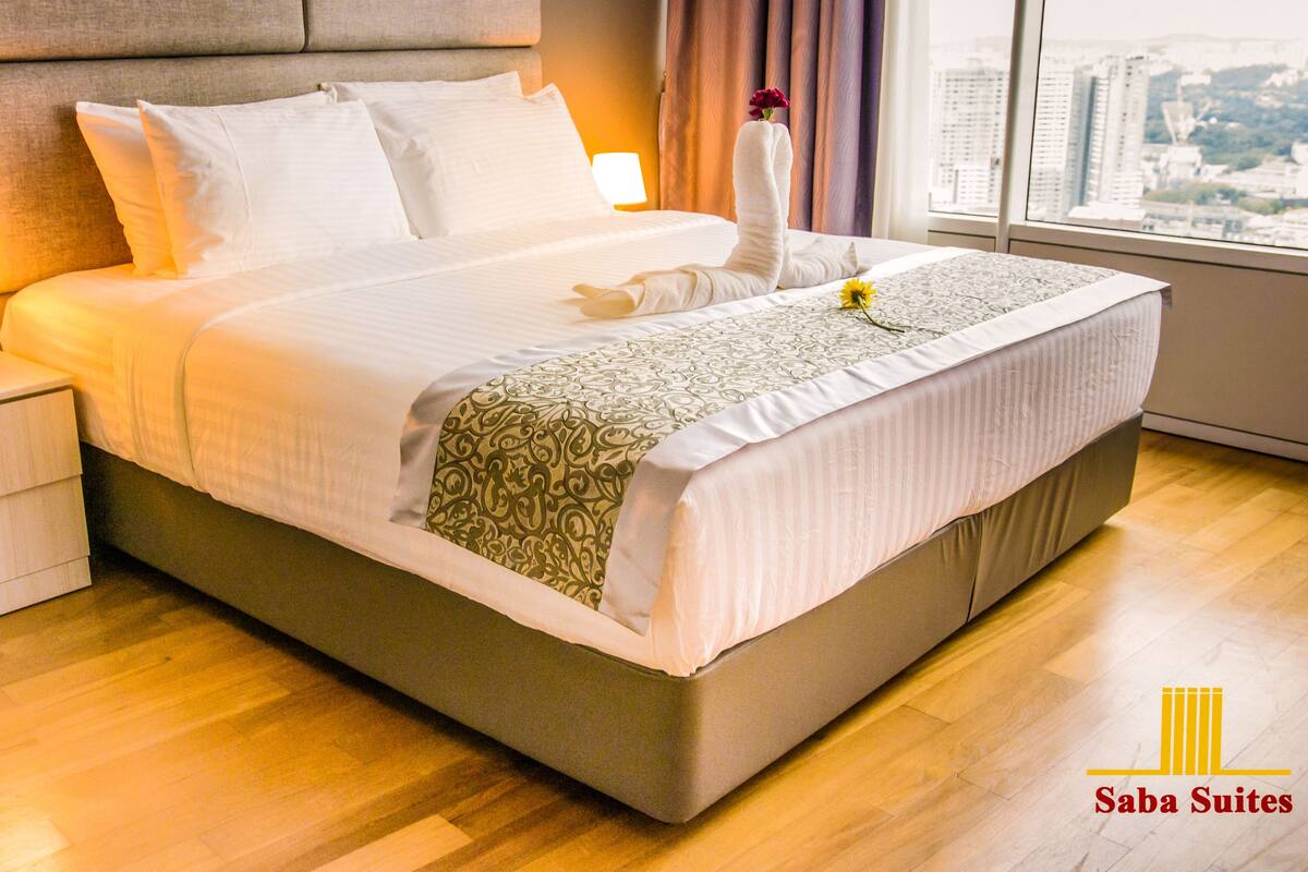 A hotel room with a large bed, a nightstand with a lamp, and a window with a city view.