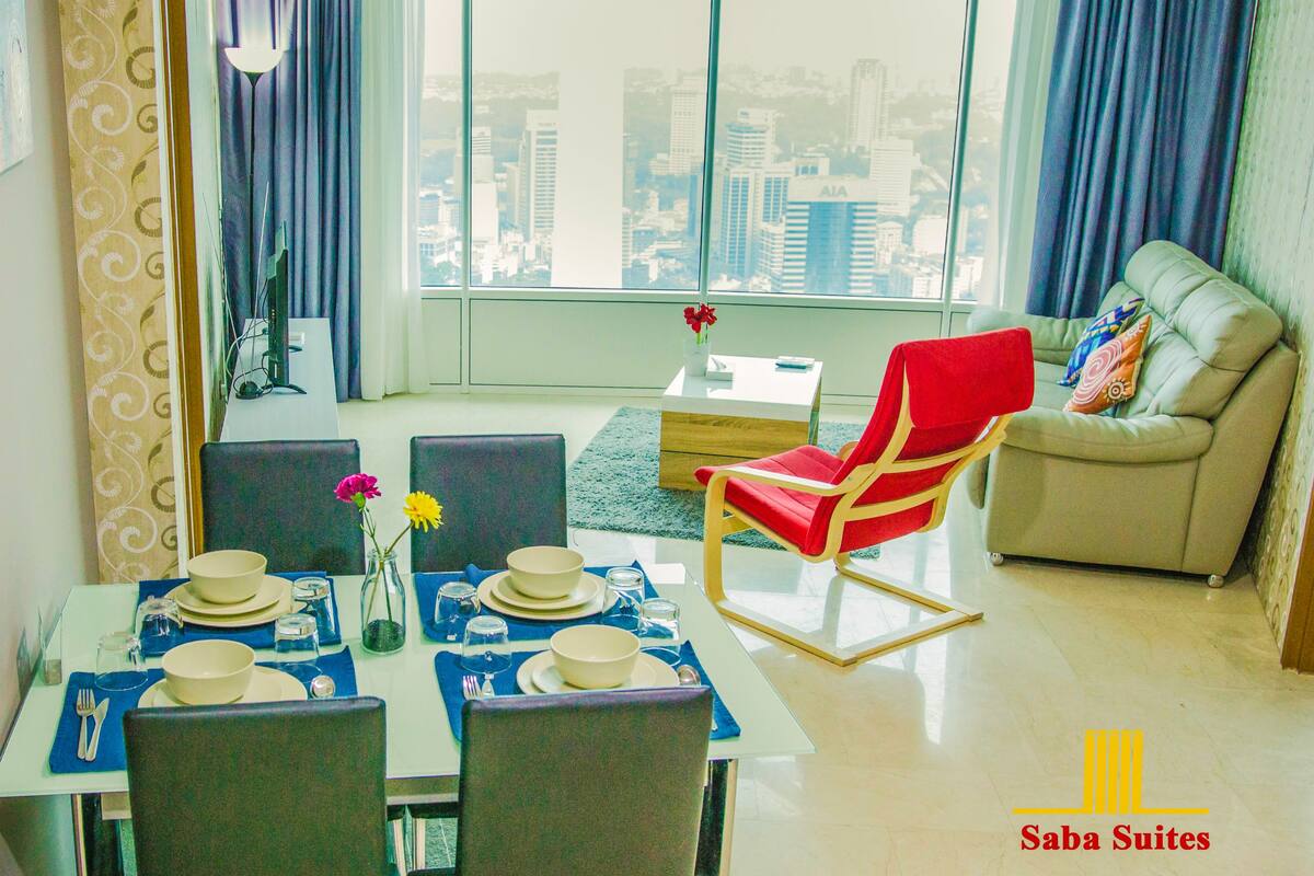 A modern living room with a dining area, large windows with a city view, a red chair, and a sofa.