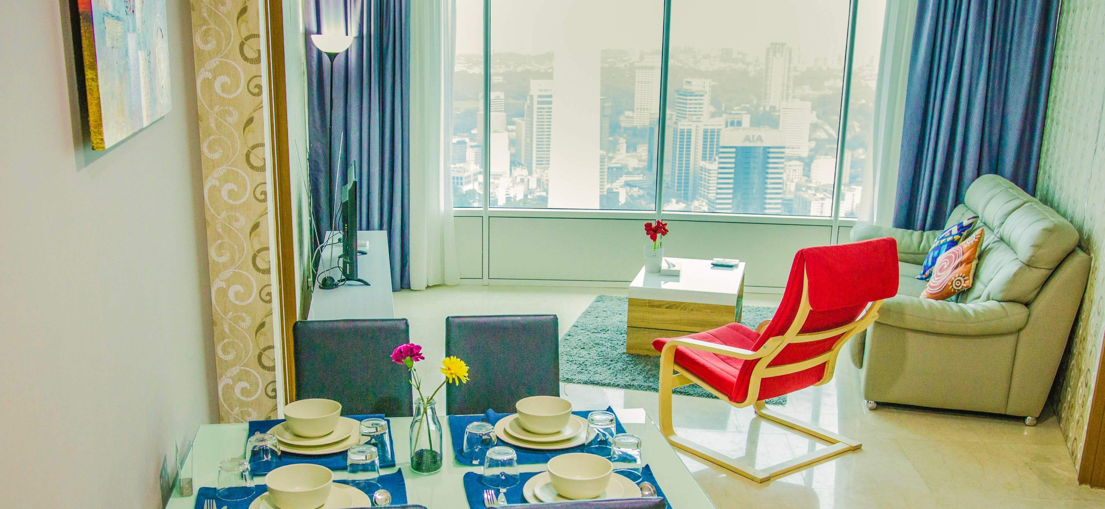 Een moderne woonkamer met een eetgedeelte, grote ramen met uitzicht over de stad, een rode fauteuil en een beige bank.