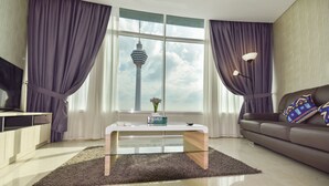 A modern living room with a glass coffee table, a sofa with patterned cushions, and a view of a tower through large windows. - Saba Suites at Vortex KLCC Bukit Bintang (Kuala Lumpur)