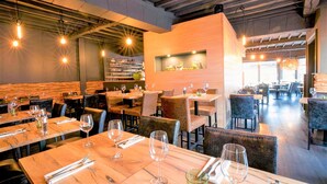 A restaurant interior with wooden tables, chairs, and hanging pendant lights. - L'Esprit Sain (Malmedy)