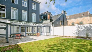 A courtyard with a covered patio, a grassy lawn, and a white wall. - L'Esprit Sain (Malmedy)