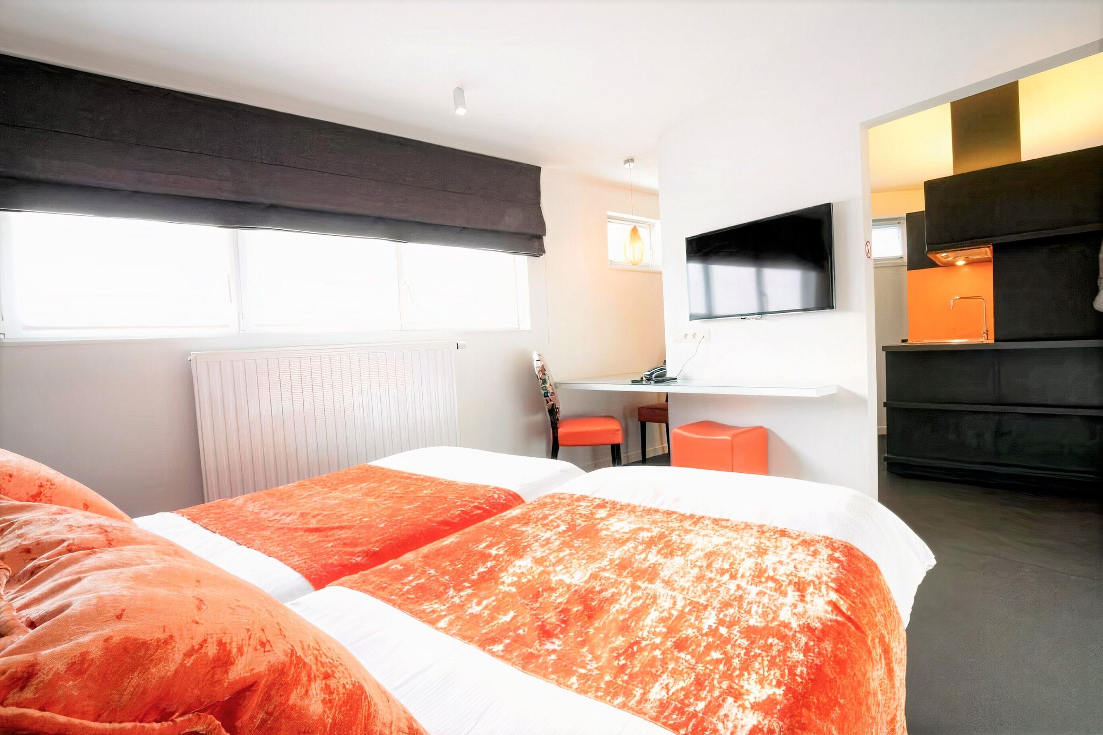 A hotel room with two beds, a TV, a desk, and a kitchenette.