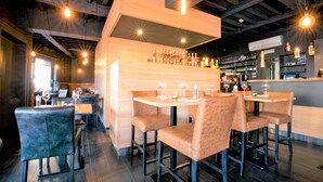 A modern bar area with high stools, a bar counter, and a variety of bottles and glasses. - L'Esprit Sain (Malmedy)