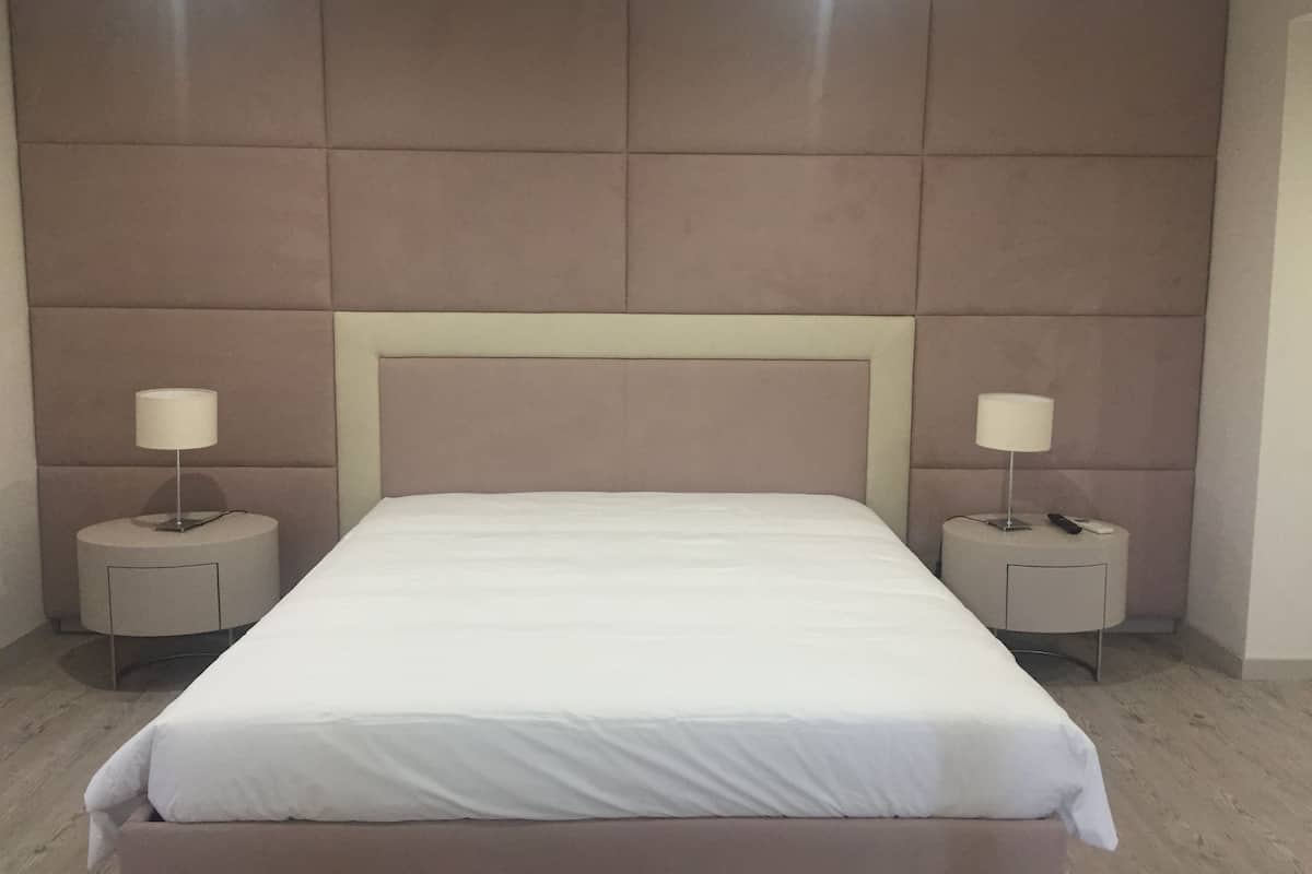 Un dormitorio con una cama grande, dos mesitas de noche y un cabecero acolchado.