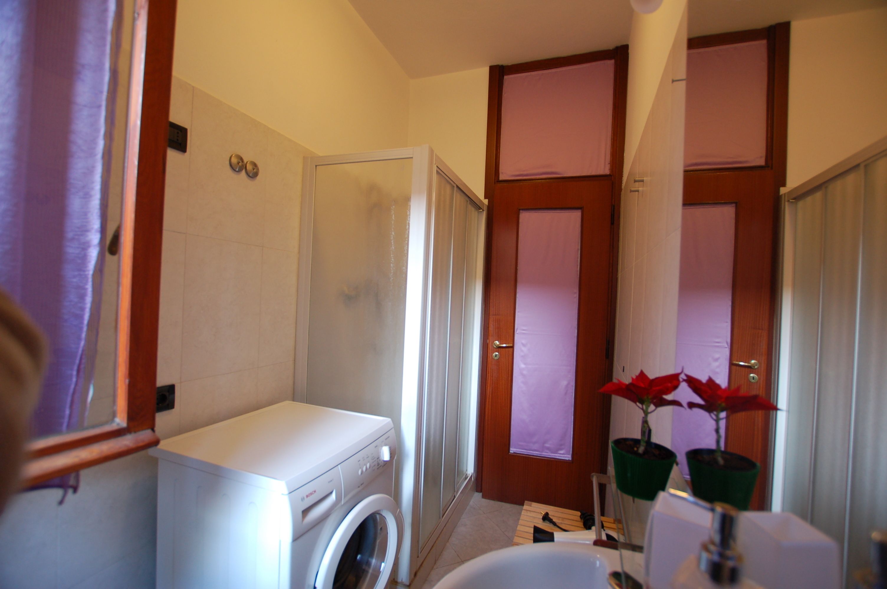 A compact bathroom with a washing machine, a shower, and a toilet.