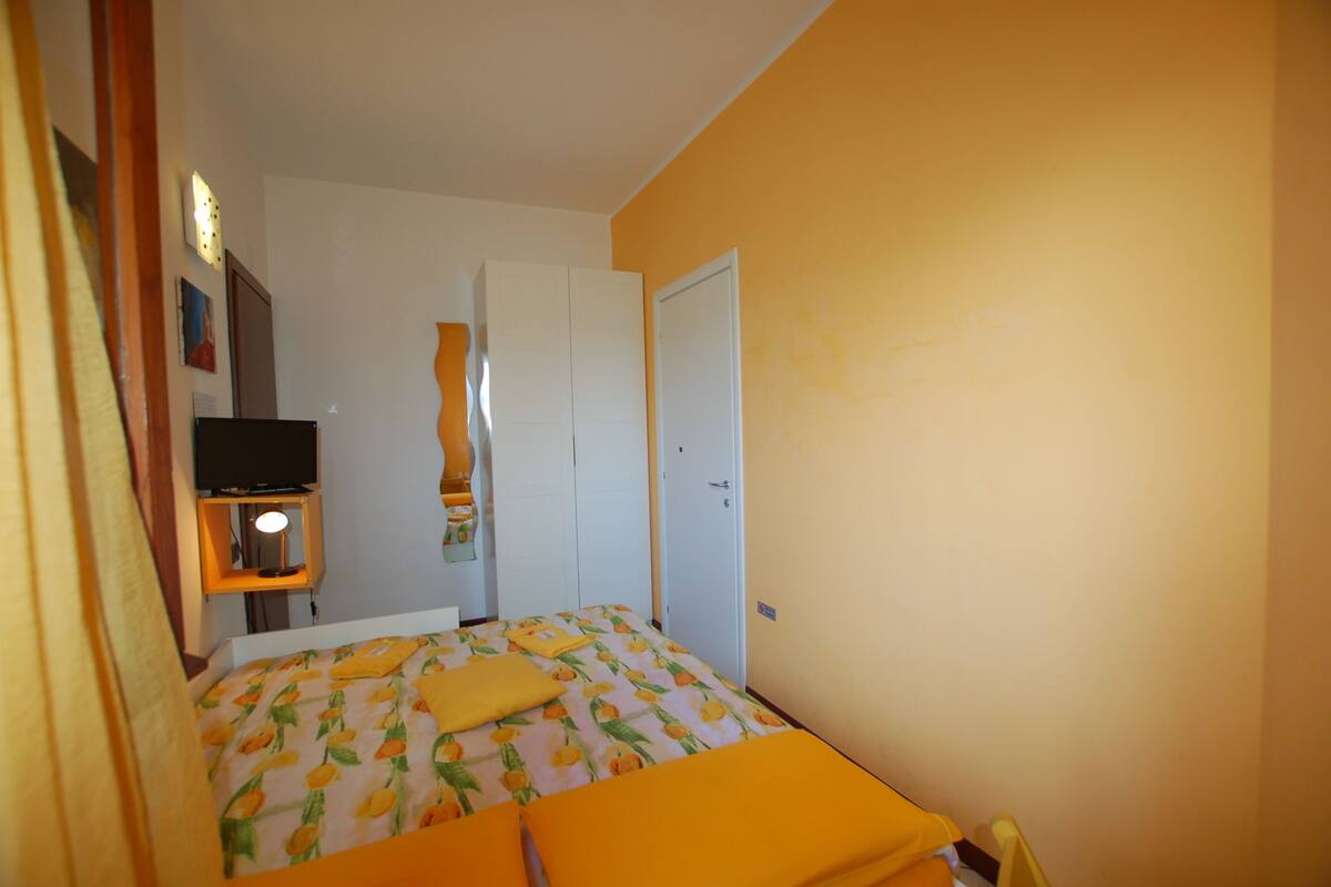 A bedroom with a bed, a television on a shelf, and a wardrobe.