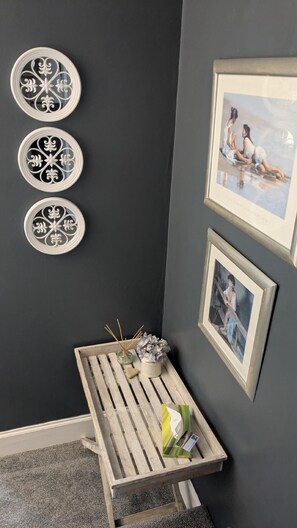 A corner room with a dark wall, three decorative plates, a framed painting, a small wooden table with a vase and candles, and a framed picture. - The Bridges B&B (Morpeth)