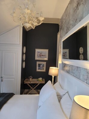A hotel room with a bed, a bedside table with a lamp, a mirror, and framed pictures on the wall. - The Bridges B&B (Morpeth)