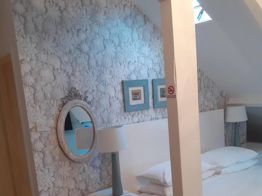 A bedroom with a white dresser, a round mirror, a lamp, and a bed. There are floral wall decorations and two framed pictures on the wall.