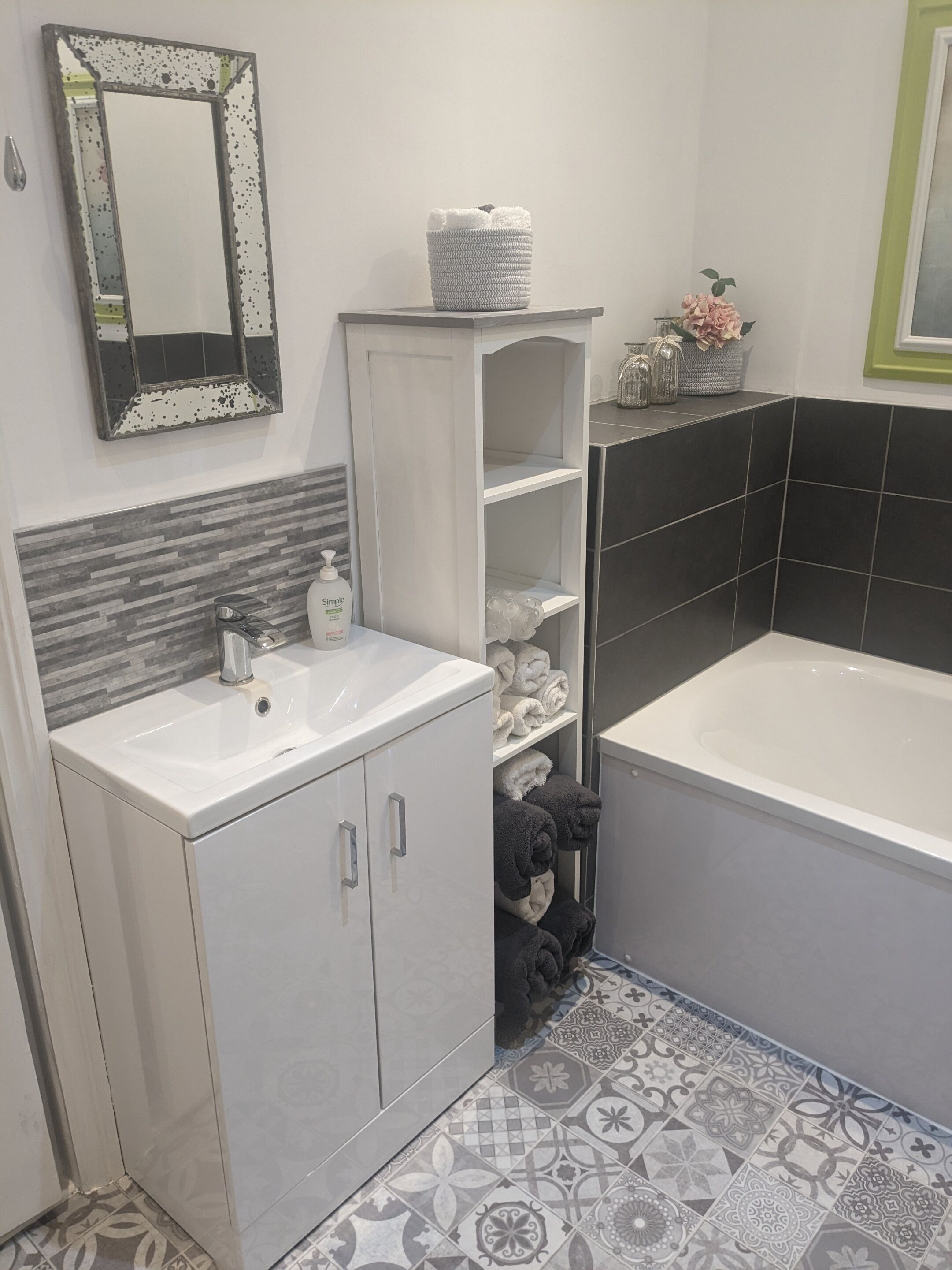 A bathroom with a white sink, a mirror, a bathtub, and a shelf with towels.
