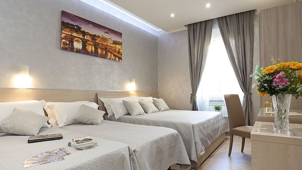 Habitación de hotel con dos camas, una mesita de noche, un florero con flores y un cuadro en la pared.