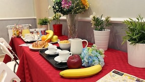 Una mesa de desayuno con mantel rojo, diversas opciones de comida, un jarrón de flores y un mapa.